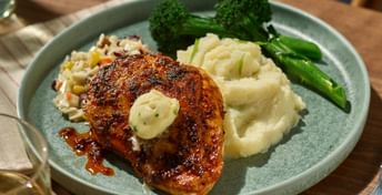White Spot's chicken breast with mashed potatoes, broccoli, and mixed vegetables on a sage green plate, served with white wine at a wooden table.