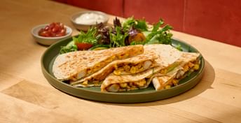 Grilled chicken quesadillas with corn and green beans served on a plate with fresh mixed greens salad and side condiments on a wooden table.