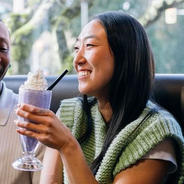 White Spot guest holding a milkshake in a booth, smiling.
