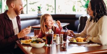 Photo of a child eating a french fry at a White Spot table looking at her parents