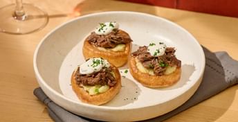 Three open-faced sandwiches topped with shredded meat and creamy sauce on toasted bread rounds, served on a white plate with a gray napkin on a wooden table.