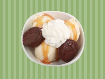 White bowl filled with vanilla ice cream, chocolate cookies, caramel sauce, and whipped cream on a green striped background.
