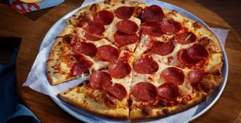 Pepperoni pizza on a white plate with one slice removed, served on a wooden table alongside a glass of beer with a coaster